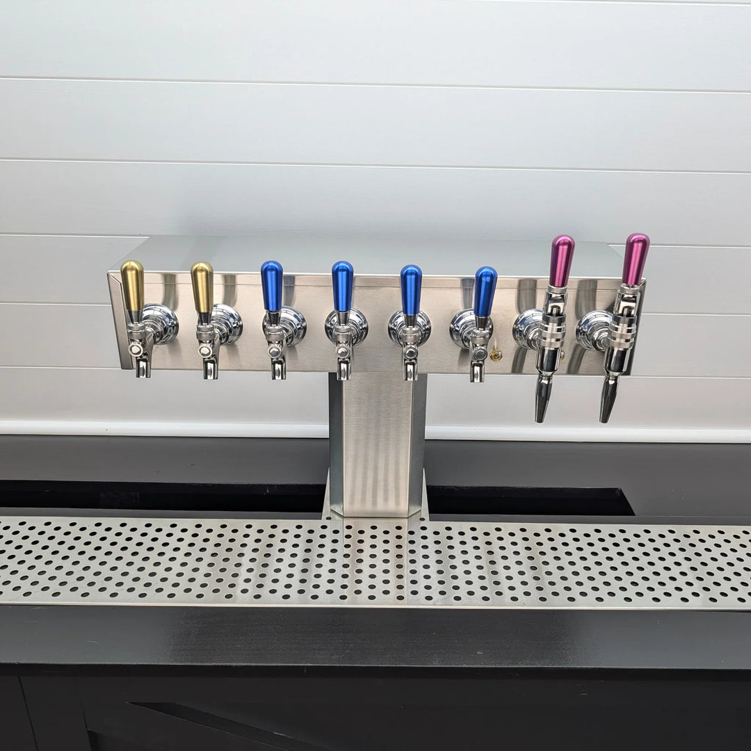 Row of beer taps on a bar counter with a white tiled wall in the background.