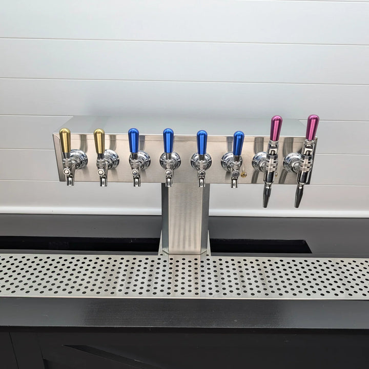 Row of beer taps on a bar counter with a white tiled wall in the background.
