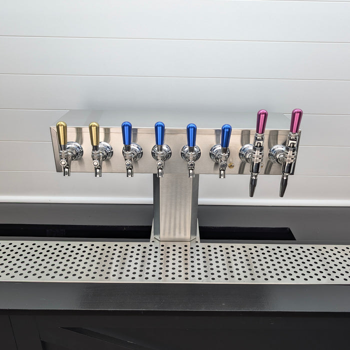 Row of beer taps on a bar counter with a white tiled wall in the background.